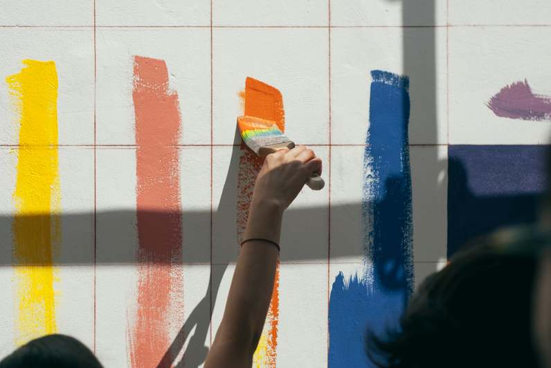 A focused painter holding a high-density foam roller beside neatly labeled paint cans and a detailed notebook